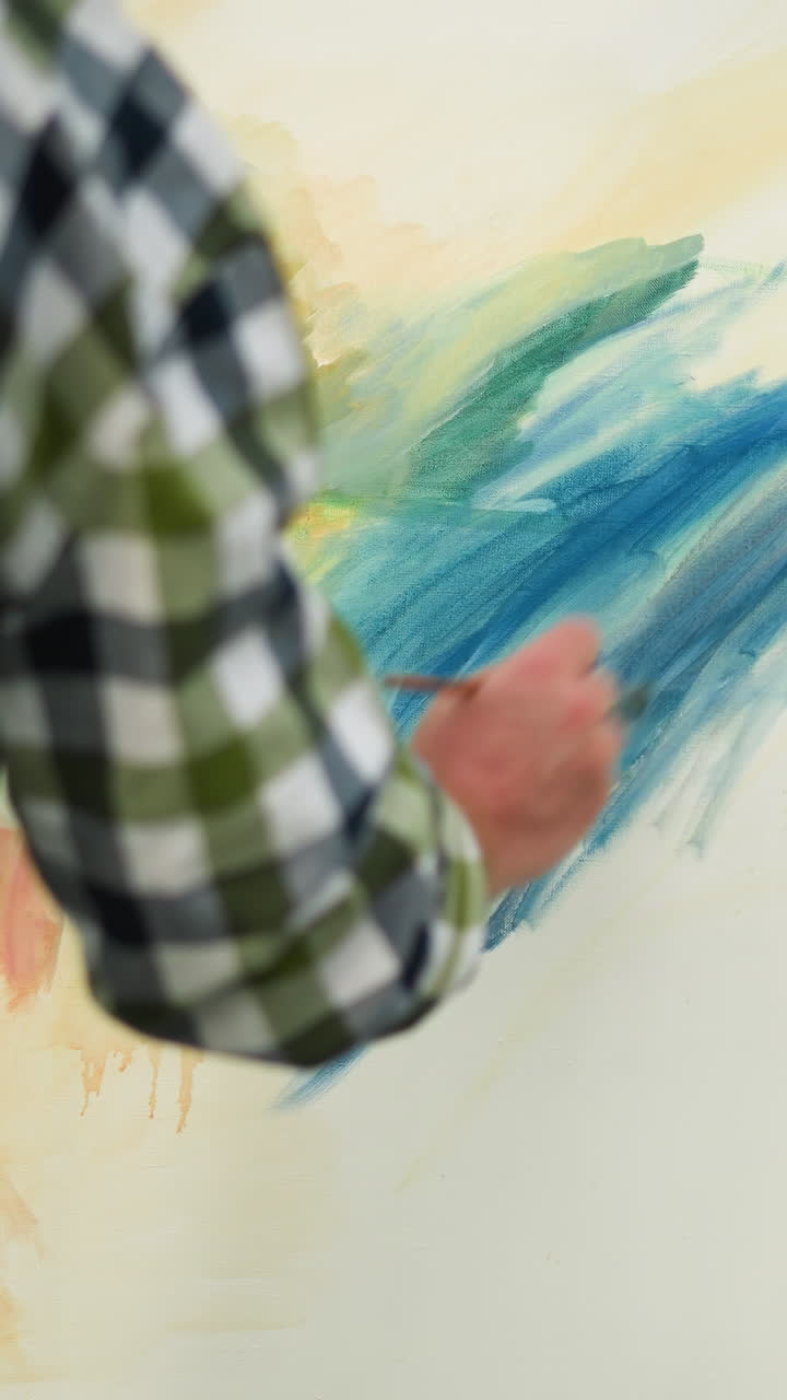 una vista trasera de un ilustrador con un sombrero negro y una camisa a cuadros, centrado en pintar un lienzo grande y colorido en un campo de hierba sereno