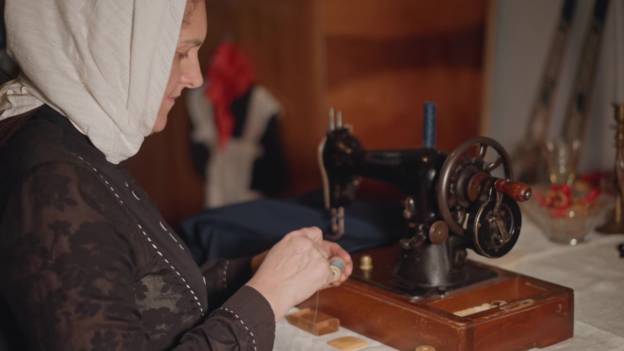 Donna anziana che infila una macchina da cucire vintage, mani ferme su rocchetto e ago, laboratorio illuminato da luce calda, sarta concentrata che ripara un indumento con punti delicati e tessuto di famiglia.