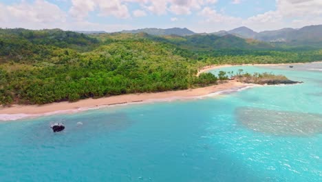 Vista-Aérea-Que-Muestra-El-Paraíso-En-La-República-Dominicana-Con-Mar-Caribeño-Turquesa,-Playa-De-Arena-Y-Paisajes-De-Colinas-Tropicales-En-Un-Día-Soleado---Ascenso-A-Gran-Angular