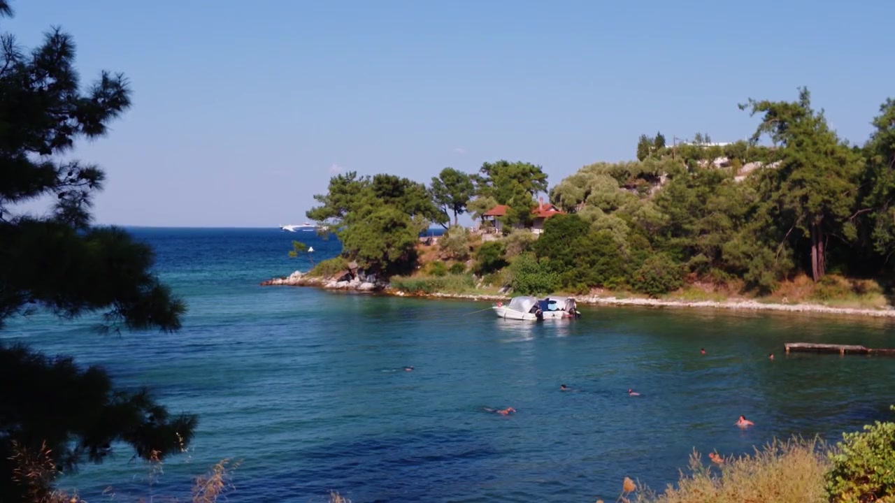 Persone che nuotano nel mare limpido e turchese vicino alla costa di Thassos, Grecia, con un piccolo yacht sullo sfondo.