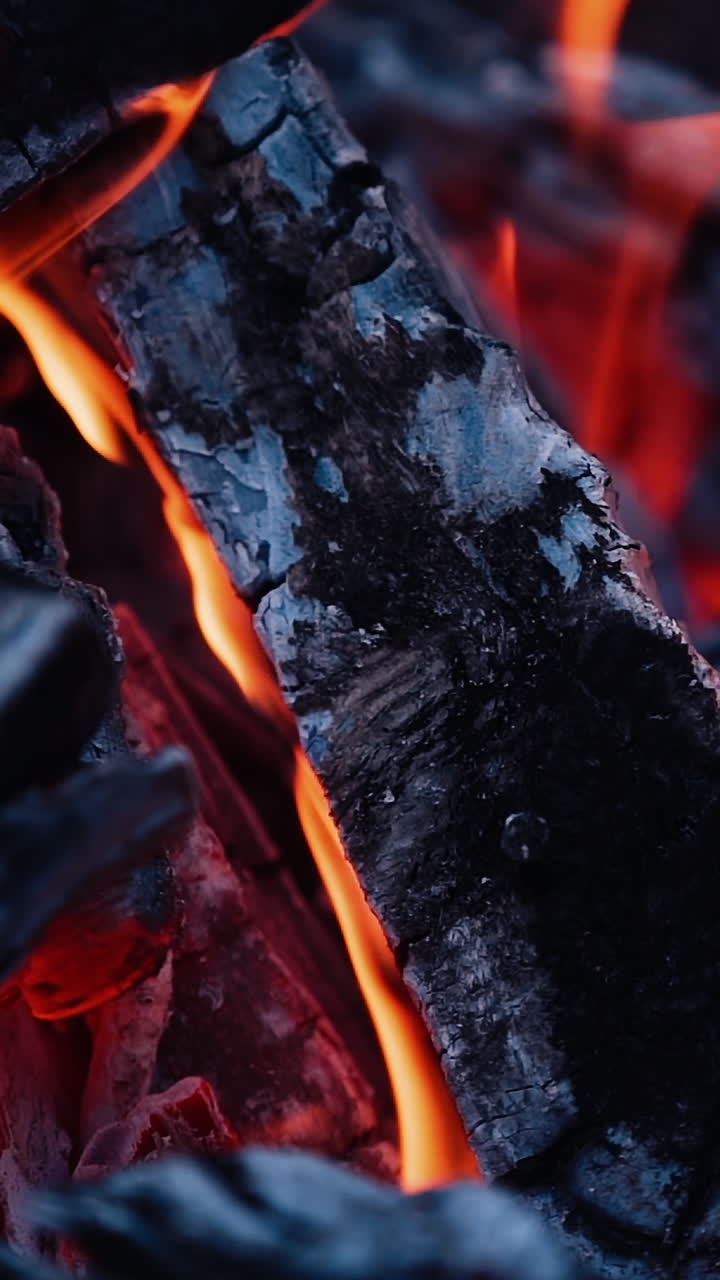 Smoldered logs in burnt fire. Dark firewood with light flame in slow motion. Close-up. Vertical video