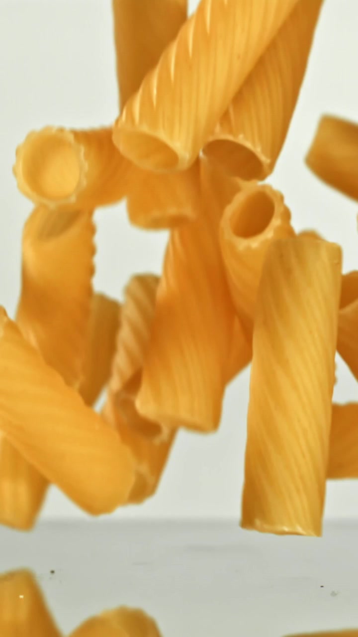 Rigatoni secchi che cadono al rallentatore su sfondo bianco