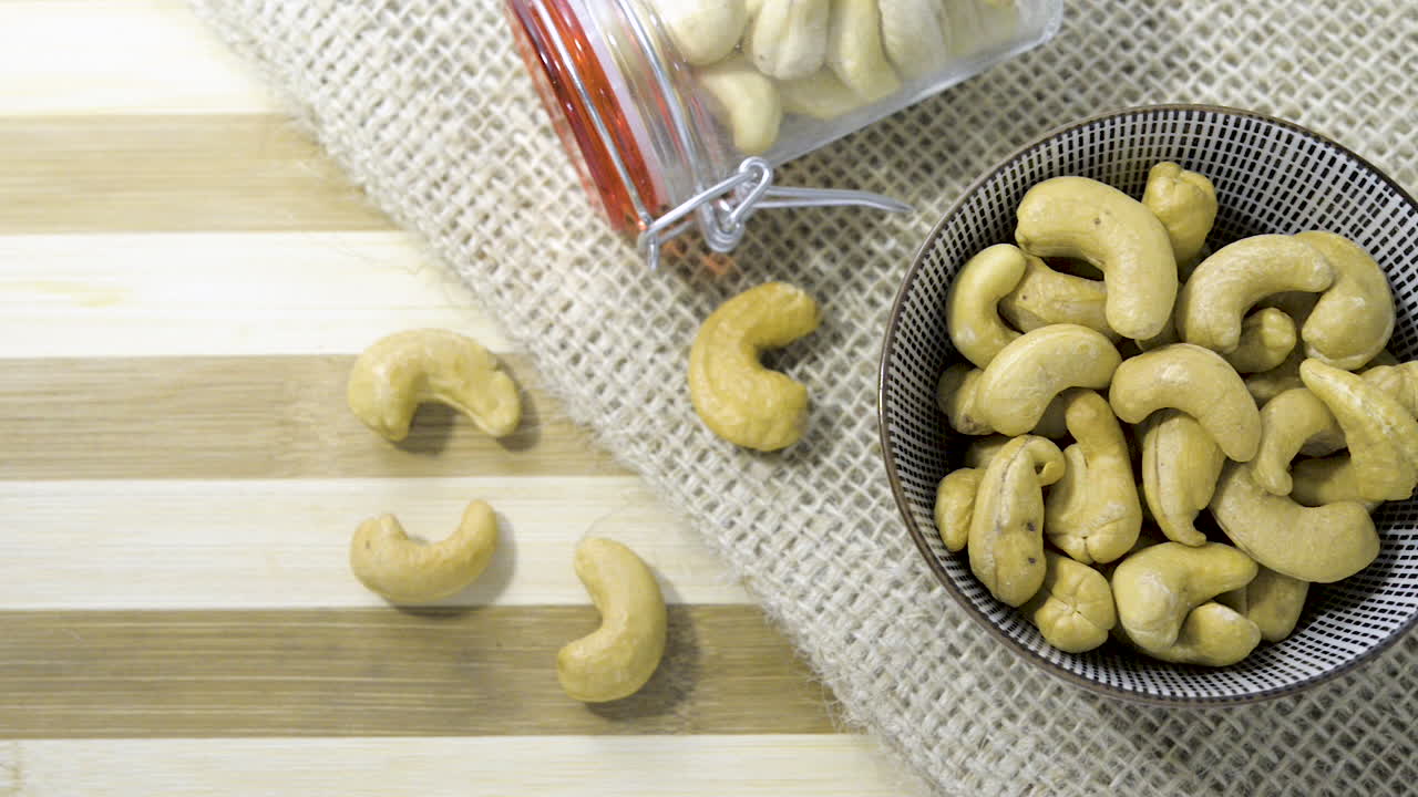toma panorámica a través de una mesa de madera a rayas, un tarro de vidrio de tela de arpillera cuenco de cerámica lleno de anacardos a la mitad