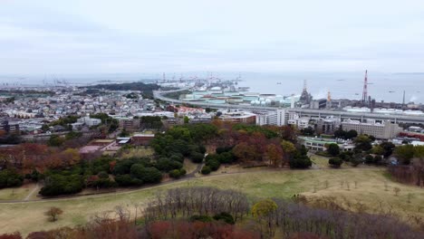 A-coastal-industrial-city-with-green-park-areas-and-overcast-skies,-aerial-view