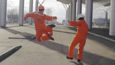 two happy construction workers in orange uniform and helmets walking and jumping together