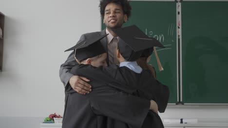 happy miltiracial students hugging their teacher. they are wearing gowns and mortarboards.