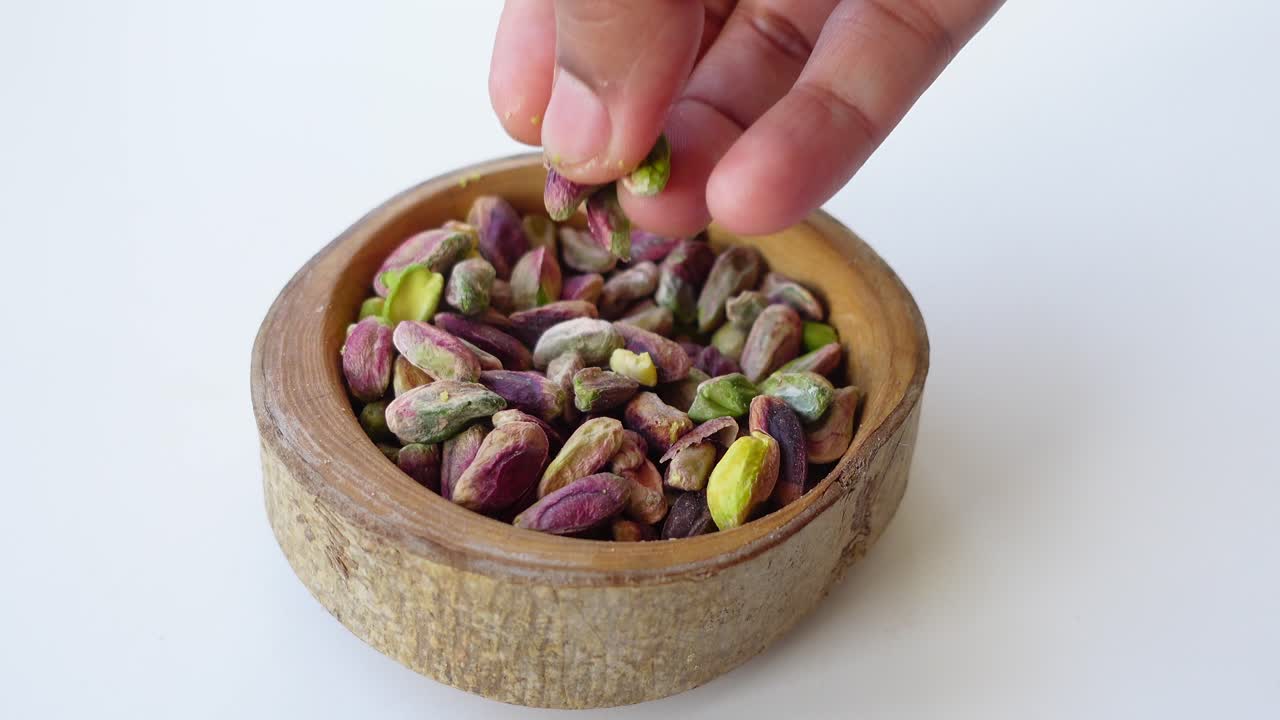 cerca de una mano que alcanza los pistachos en un cuenco de madera