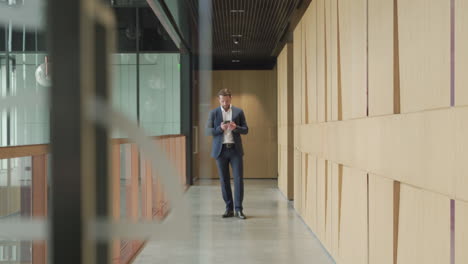 an attractive young, bearded businessman in a blue suit has a business conversation as he enters the offices through a modern wooden hallway