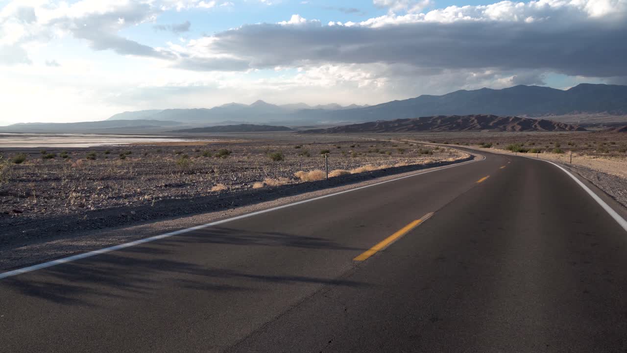 Autostrada solitaria con curva che attraversa la Valle della Morte, deserto del Mojave, California. Ripresa dolly a sinistra