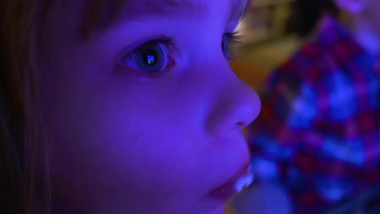 Primo piano di una bambina che si riempie la bocca di popcorn mentre guarda la televisione.