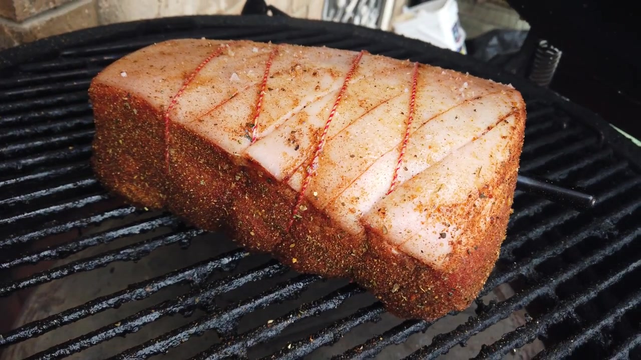 Krydret svinekam med ridset fedtkant bundet med slagtersnor, der langsomt ryger på en rund grill til et havemåltid.