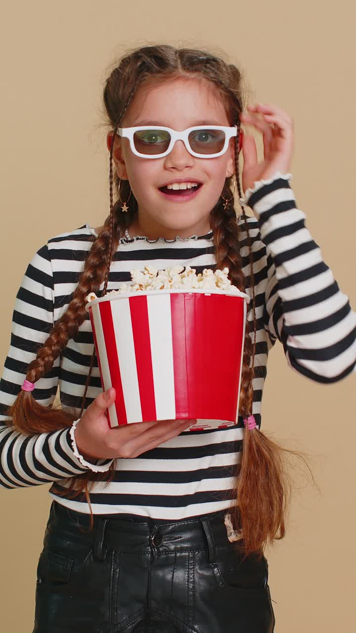 Excited amazed child girl kid eating popcorn watching online movie film wearing 3d cinema glasses