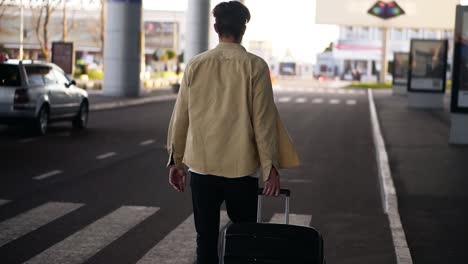 confident, tall man in casual with the black baggage walking to the outside airport terminal by road. slow motion. rare view