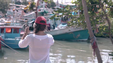 chica con gorra dispara en el puerto con barcos de pesca asiáticos atrás