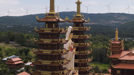 orbital shot of buddhist temple with two pagoda towers and wind turbines, aerial closeup