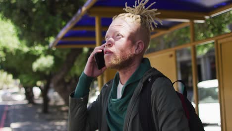 Happy-albino-african-american-man-with-dreadlocks-in-park-talking-on-smartphone