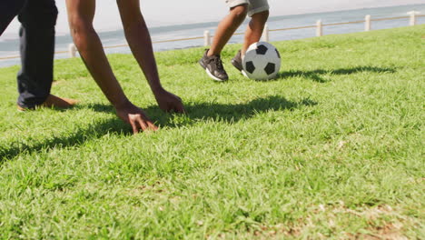 video of legs of african american father and son playing soccer outdoors and having fun