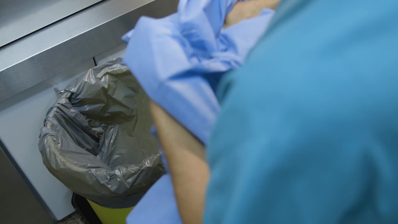 A male nurse throwing away his operating clothes into a bin.