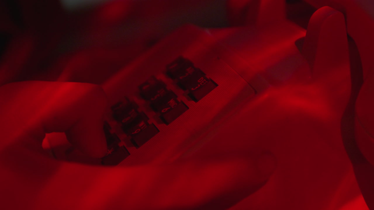 мужчина набирает номер телефона, чтобы сделать телефонный звонок на классическом белом столовом телефоне в комнате с красным светом