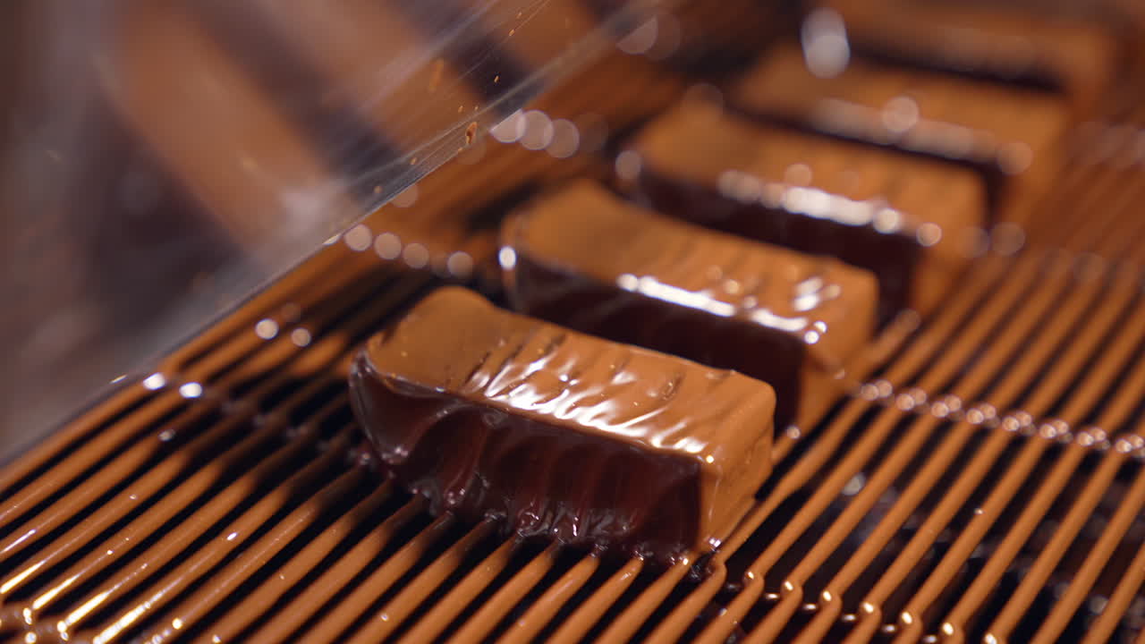 Sweets are poured with chocolate and blown by the airflow. Little waves of chocolate roll along the candies close up. The production line at a candy factory.
