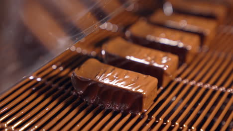 sweets are poured with chocolate and blown by the airflow. little waves of chocolate roll along the candies close up. the production line at a candy factory.