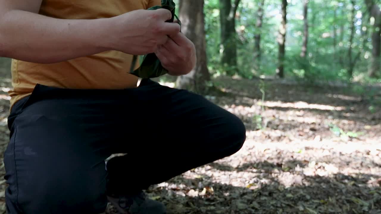 Tourist puts tent anchors in a bag, tie it and prepare to leave the forest campsite