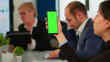 businesspeople analysing reports sitting at desk, while employee holding phone with green screen