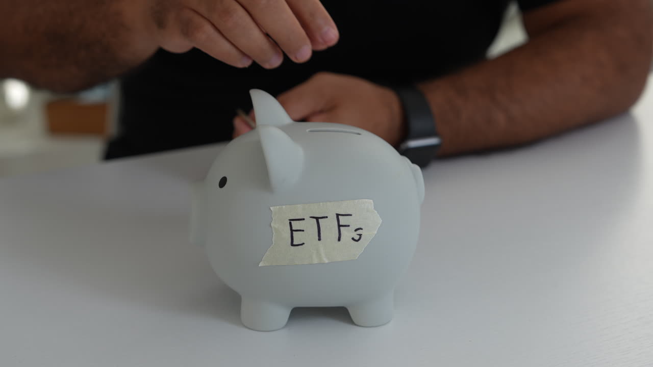 Uno scatto ravvicinato di una persona con un salvadanaio etichettato ETFs su un tavolo bianco, sotto un'illuminazione soffusa, che cattura un senso di finanza personale e risparmio per investimenti.