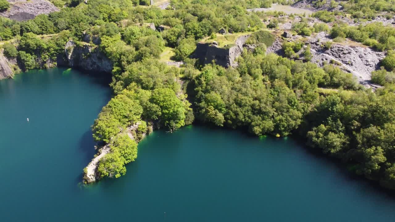 Cava di ardesia dismessa e ricoperta di vegetazione di Dorothea in un lussureggiante e fitto bosco montano di Snowdonia, vista aerea con inclinazione verso il lago