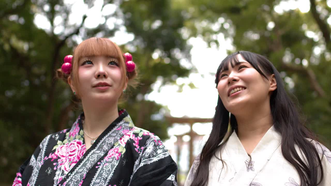 花柄の着物を着た友人二人が、日本の森の神社で屋外にて談笑し、微笑み合っている。