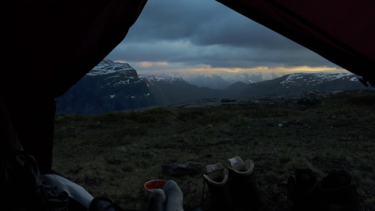 Person without shoes camping on Trolltunga, motion back view to tent