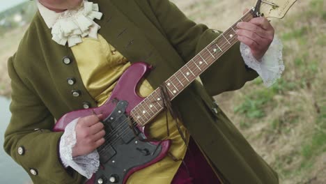 man in historical costume playing electric guitar by a river