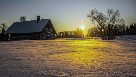 golden sunrise reflecting on a field of fresh snow and a cabin in the countryside - time lapse