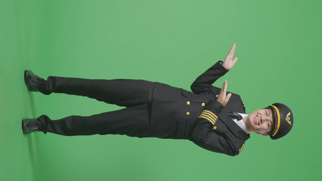 녹색 스크린 배경 스튜디오에 서 있는 동안 웃고 을 가리키는 아시아 남자 조종사의 몸이 가득 차 있습니다.