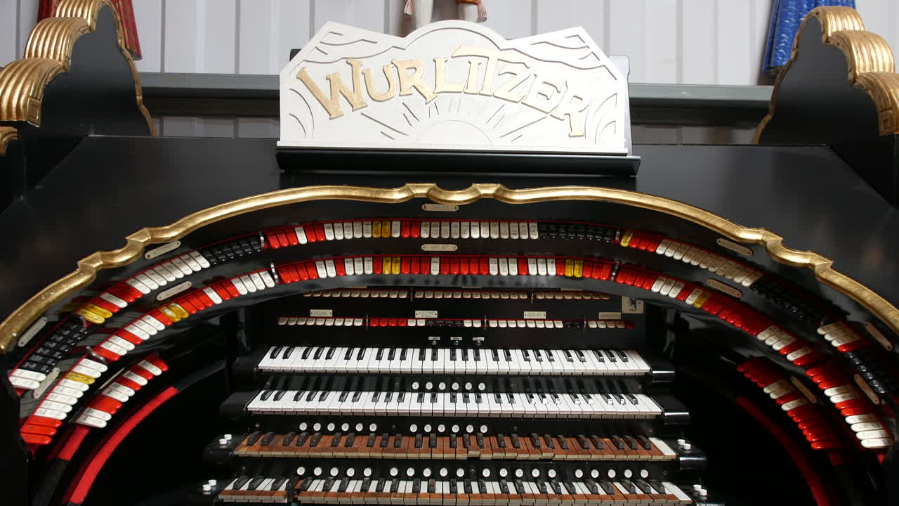 An organ labeled Wurlitzer is displaying multiple keyboards stop tabs and curved rows of controls framed in gold trim within a black wooden structure
