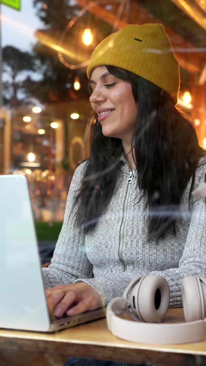 Giovane donna felice che lavora al laptop e beve caffè al bar