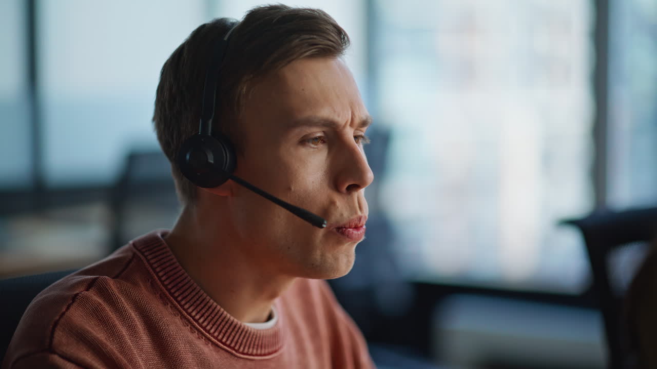 Serious helpdesk assistant talking headset in office coworking space closeup