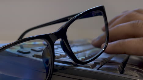 eyeglasses resting on keyboard with hands typing