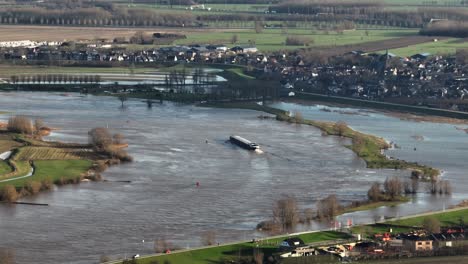 aerial panning shot of the lek river overrunning its banks with the town of nieuwegein in the background and a freighter trying to make its way along the river