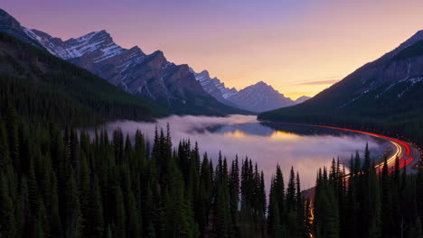 misty lake and mountain range at dawn with highway light trails