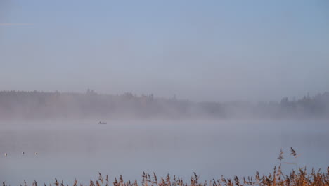 morning fog hazy peaceful lake with small fishing boat, autumn stillness