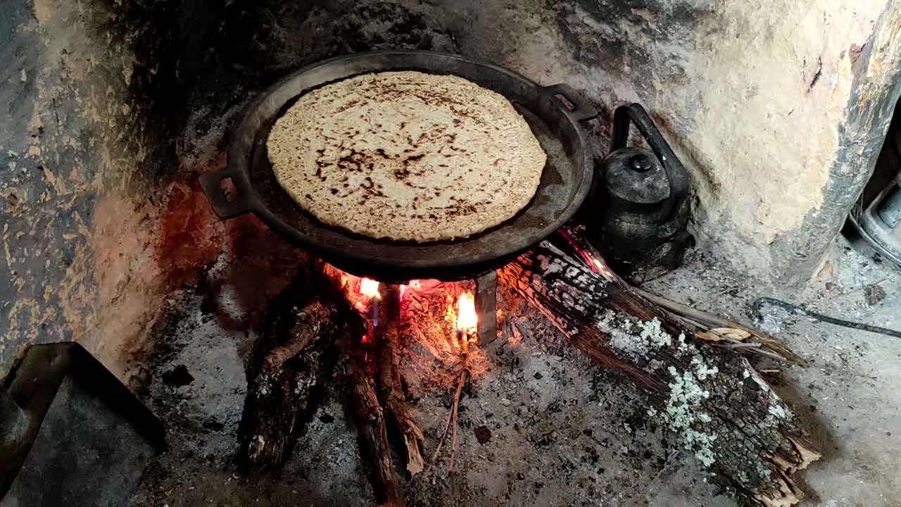 primer plano de cocinar pan en una sartén de hierro fundido descansando sobre salvamanteles, sobre un fuego de madera de roble en una gran chimenea de piedra en una cocina tradicional-3