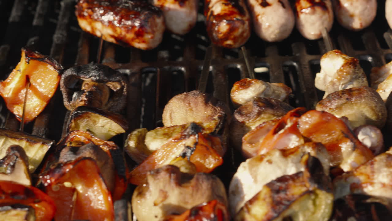 visión general de la barbacoa completa con hamburguesas de carne de res, salchichas de cerdo y kebabs de vegetales con humo que se eleva desde el carbón