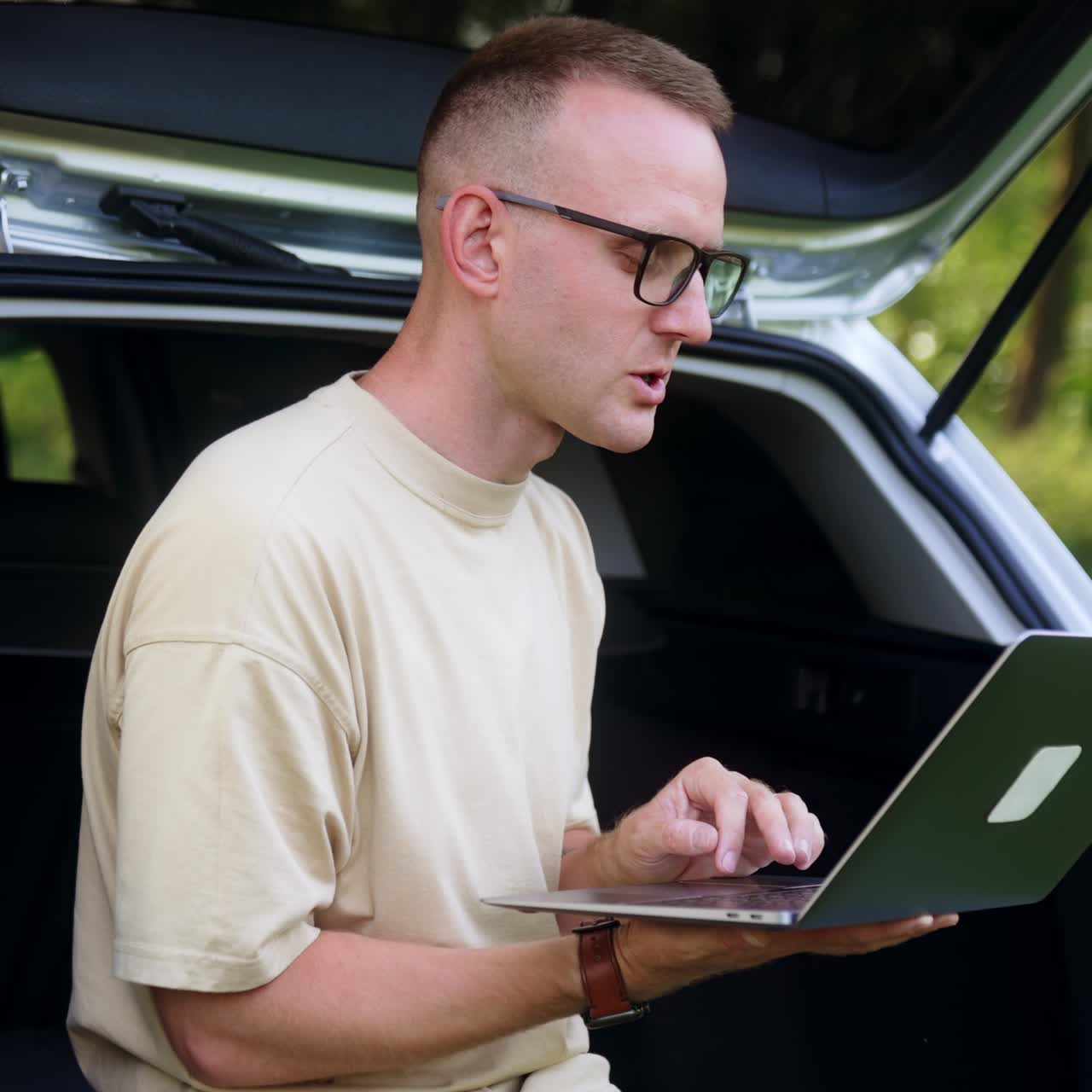 Mid-aged freelancer focused on laptop. Man works sitting in car trunk in the forest