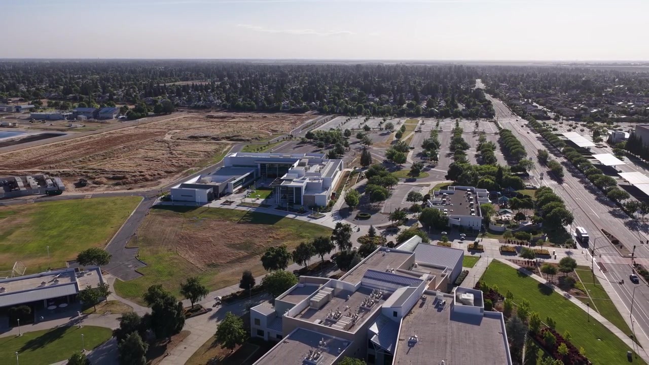 Ampia veduta aerea del campus del Clovis Community College a Fresno, California, che mostra architettura moderna, prati verdi, un ampio parcheggio e il paesaggio suburbano circostante.