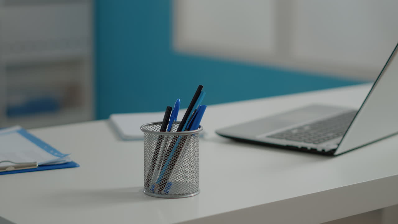 Close up of pens and laptop on white desk in empty cabinet