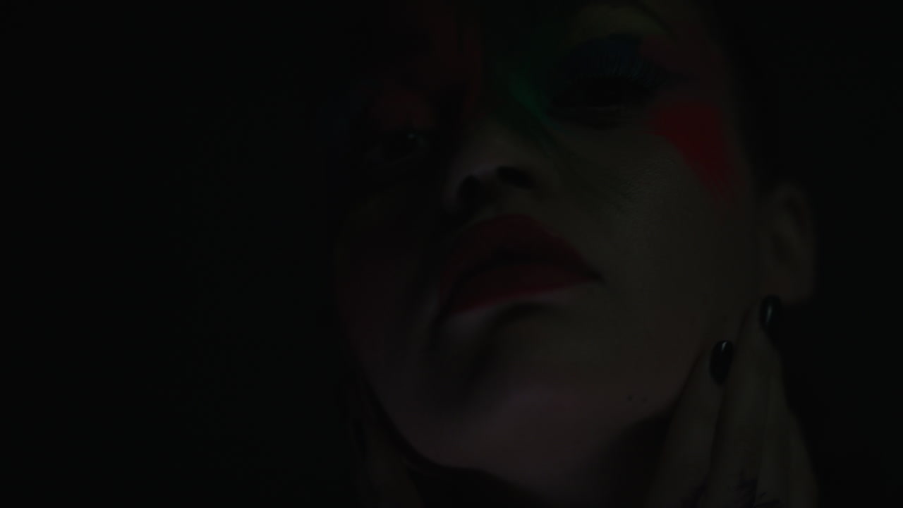 retrato de cerca de una mujer hermosa con una pintura de rostro colorida bailando arte corporal multicolor exótico con destellos de luz