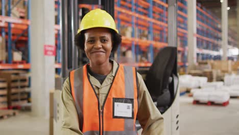 portrait of african american female worker wearing safety suit and smiling in warehouse