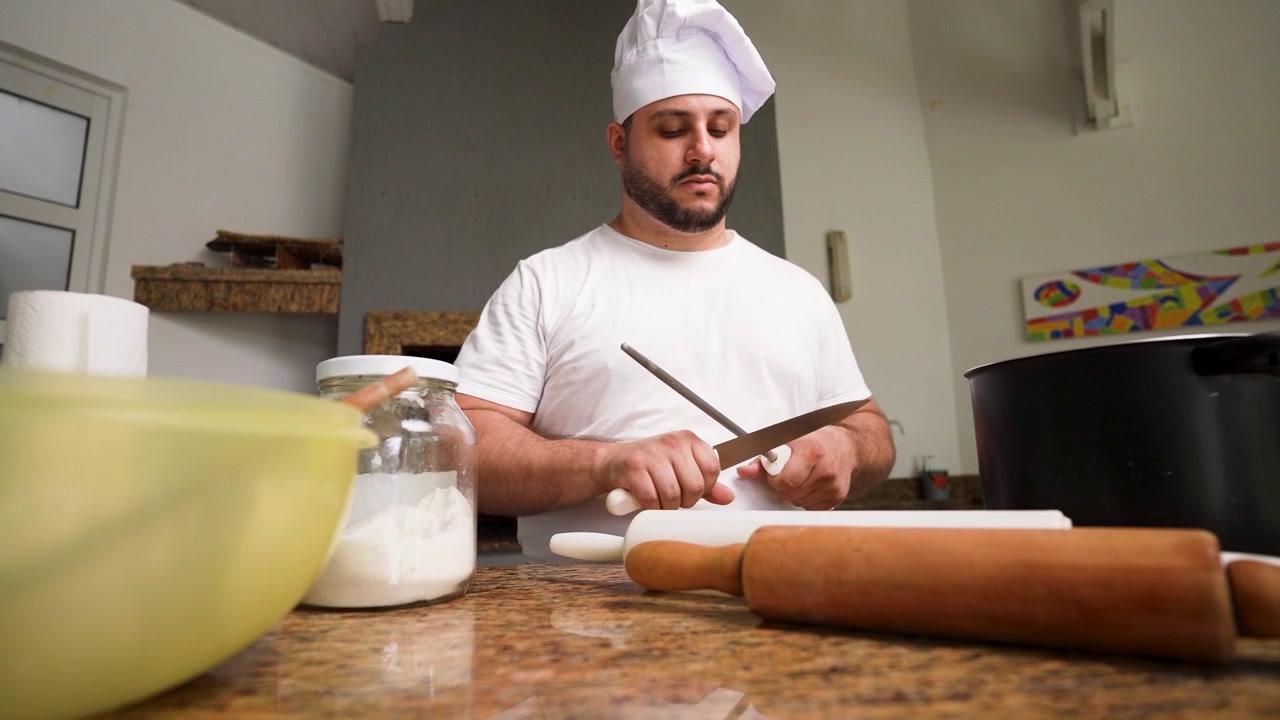 Ein Koch schärft sorgfältig verschiedene Messer auf einer Arbeitsplatte, um sicherzustellen, dass seine Werkzeuge in bestem Zustand zum Kochen sind.