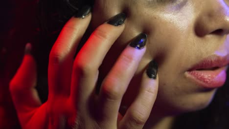 woman scratches her face with black nails, in a dark atmosphere, showing pain